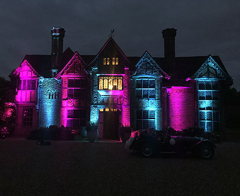 Mansion exterior lit at night in magenta and cyan light.